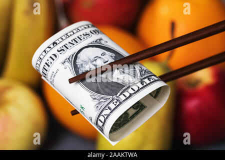 Konzept zum Thema der wirtschaftlichen Konfrontation zwischen Amerika und China. Essen Embargo. Chinese sticks halten einen Dollar auf einem Hintergrund von Obst, c Stockfoto