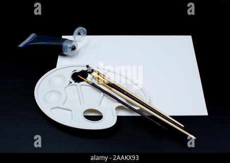 Farbpalette mit schwarzer Acrylfarbe, Pinsel und Leinwand auf schwarzem Hintergrund Stockfoto