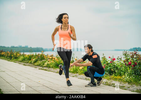 Die Ausübung durch den Fluss mit Personal Trainer. Stockfoto