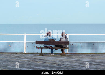 Ein Mann und eine Frau sitzen auf einer Bank sprechen, während sie auf das Meer schauen. Liebe Schlösser sind an das Geländer vor Ihnen angebracht werden. Stockfoto