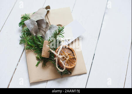 Handwerk Umschlag auf weißen Holzschreibtisch. Dekoration von tannenzweigen, Orangenscheiben und Verpackung cinnamonNew Jahr Idee Stockfoto