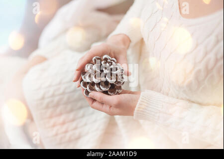 Ein Mädchen in einem weißen Strickpullover hält einen Kegel. Selektive konzentrieren. Stockfoto