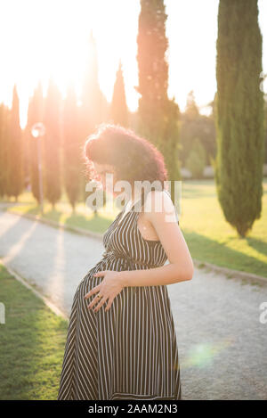 Schwangere Frau ihren Bauch berühren in Park Stockfoto