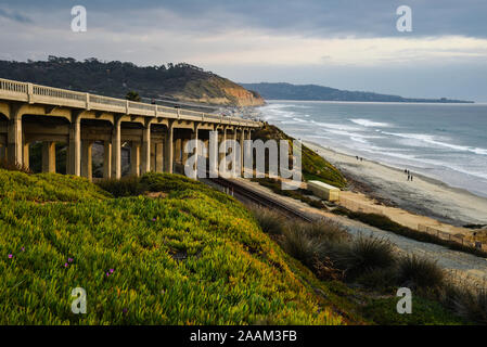 Torrey Pines Road auf der Brücke, Eisenbahnschienen unter, neben Sandstrand mit Wellen am Ufer bei Sonnenuntergang brechen, La Jolla, Kalifornien, USA Stockfoto