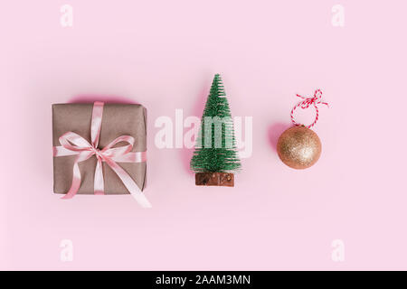 Miniatur Weihnachtsbaum, Geschenk verpackt in Handwerk Papier und Weihnachtsbaum Kugel Dekoration auf rosa Hintergrund. Stockfoto
