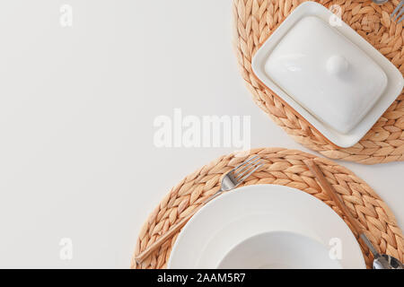 Weißer keramik geschirr, Fibre geflochtene runde Tischset, Besteck und auf butterdish weißen Hintergrund. Im skandinavischen Stil. Stockfoto