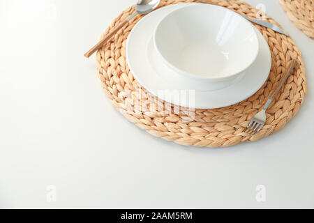 Weißer keramik geschirr, Fibre geflochtene runde Tischset und Besteck auf weißem Hintergrund. Im skandinavischen Stil. Stockfoto