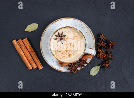 Indische Masala Chai Tee. Traditionelle indische heißen Getränk mit Milch und Gewürzen auf dunklem Stein Tabelle Hintergrund. Ansicht von oben, flach. Stockfoto