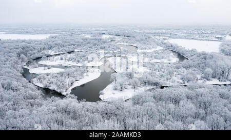 Eine Drone / Luftaufnahme eines windigen Flusses, umgeben von schneebedeckten Bäumen, mit Wolken über der Spitze schweben. Stockfoto