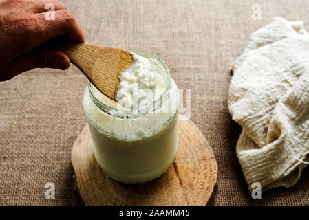 Die Hand des Mannes gießt Milch Kefir in eine Kanne ein gesundes Frühstück für die intestinale Mikrobiota vorzubereiten. Stockfoto