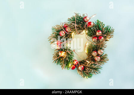 Weihnachten runden Kranz aus Fake grünen Zweigen und roten Beeren, die in Gold an den Spitzen gemalt, Weihnachtsbeleuchtung, wickeln Sie einen Kranz auf hellen Stockfoto