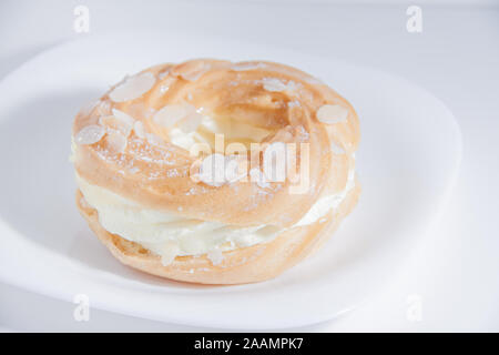 Ring donut Schnitt in der Mitte und innen Schlagsahne und auf die Oberseite Mandelblättchen und Zucker Puder auf weiße Platte auf hellen Hintergrund mit Platz für Stockfoto