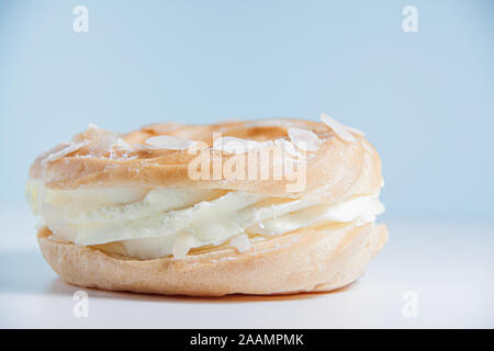 Ring donut Schnitt in der Mitte und innen Schlagsahne und auf die Oberseite Mandelblättchen und Zucker Puder auf hellblauem Hintergrund. Stockfoto