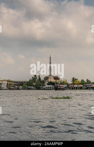 Cai, Mekong Delta, Vietnam - März 13, 2019: Entlang der Kinh 28 Kanal. Porträt der Katholischen Kirche hinter Reihe von Einzelhandelsunternehmen und grünen Folia Stockfoto