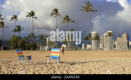 Honolulu, Hawaii, USA - 10. Juni 2015: Blick auf zwei Liegen auf der magischen Insel Lagoon Beach mit Blick auf die Skyline von Honolulu im Hintergrund Stockfoto