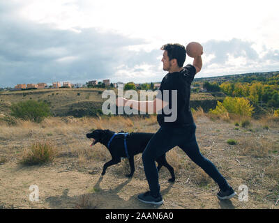 Latin junger Mann Werfen einer Kugel zu einem schwarzen Labrador Hund, Madrid Spanien. Stockfoto