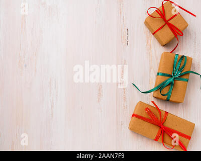 Drei Geschenkboxen aus Kraftpapier mit Bändern auf weißem Holz- Hintergrund, Ansicht von oben. Shopping, Valentines Tag Stockfoto