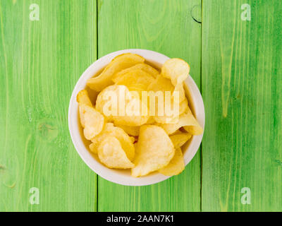 Kartoffelchips in Weiß Schüssel auf Holztisch, helles Grün Stockfoto