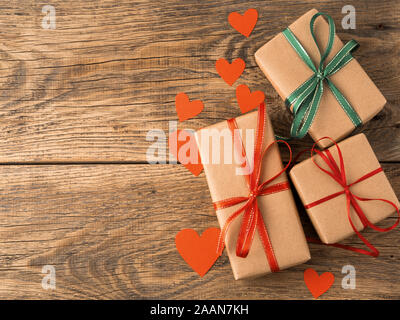 Valentinstag Hintergrund. Geschenke verpackt mit Kraftpapier braun Papier, mit roten Bändern, Herz im Alter von rustikalen Vintage alte hölzerne Hintergrund Stockfoto