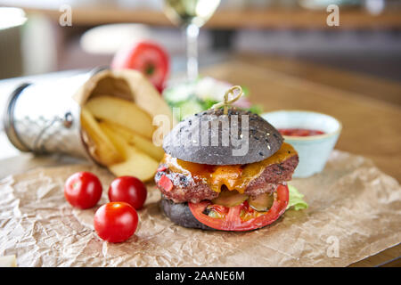 Cheeseburger mit Salat, Tomaten, Pommes frites und geschmolzenem Käse. Der Tisch im Restaurant. Ungesunde Lebensmittel. Stockfoto