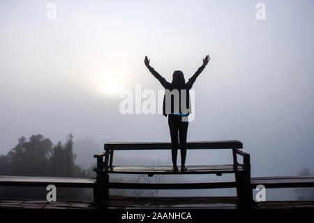 Das Bild hinter den Frauen ihre Arme auf einen hölzernen Stuhl Hintergrund Nebel und Morgensonne. Stockfoto