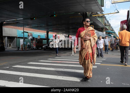 Eine Frau in ethnische Kleidung Sonnenbrillen tragen, Spaziergänge auf Roosevelt Ave, unter der erhöhten U-Bahn. In Jackson Heights, Queens, New York City Stockfoto