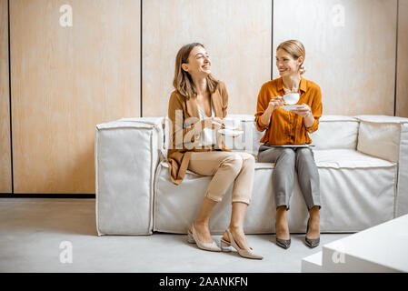 Zwei weibliche Kollegen Spaß Unterhaltung, zusammen sitzen auf der Couch bei einer Kaffeepause im Büro Stockfoto