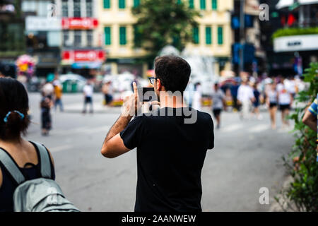 Eine stolze und glückliche kaukasischen Vater seine Söhne Tanz Performance auf einem Smartphone in einer asiatischen Stadt an einem heißen Tag Stockfoto