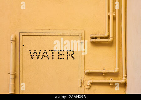 Alte wasser Metallrohre mit Halterungen vor einem Putz an der Wand mit Metall Box für Wasserzähler festgesetzt Stockfoto