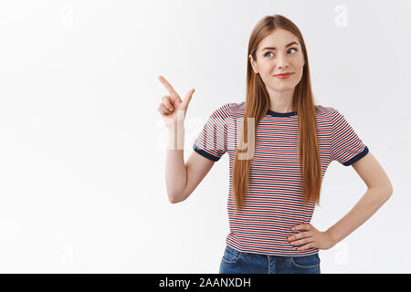 Beeindruckt , gut aussehenden Kaukasier Frau in gestreiften T-Shirt, Kippen, Kopf und grinsen amüsiert, linke obere Ecke suchen, überprüfen Sie heraus Stockfoto