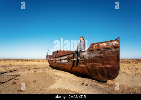 Mann sitzt auf dem Boot in der Wüste in der Nähe von Akbasty im Aralsee oder Aral See, Kasachstan Stockfoto