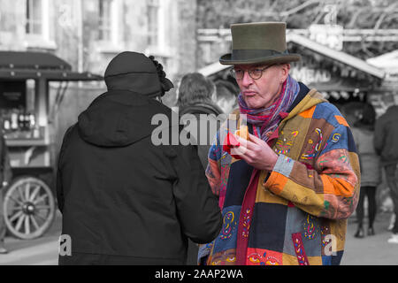 Mann mit Hut und bunten Jacke bummeln Winchester Weihnachtsmarkt, während an der Winchester, Hampshire, UK Essen im Dezember Stockfoto