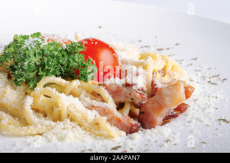 Typische Spaghetti alla Carbonara mit rohem Ei und Speck. auf einem weißen Teller mit geriebenem Pecorino. Eingerichtet mit Cherry Tomaten und parsle Stockfoto