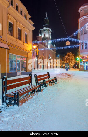 Uzhhorod, Ukraine - 06 Jan, 2019: Winter Nacht in der Stadt. Wunderschöne blaue und gelbe Weihnachtsbeleuchtung. Leere Voloshyna Straße im Schnee bedeckt. Cath Stockfoto