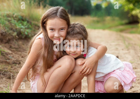 Porträt von zwei süße kleine Mädchen umarmen und lachend an den Wald. Happy Kids im Freien Stockfoto