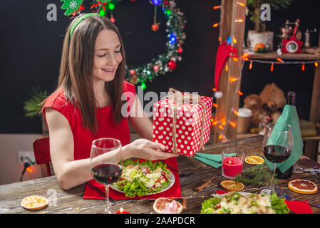 Schöne junge Frau im Urlaub Tisch mit roter Geschenkbox in Weihnachtsschmuck. Neues Jahr Stimmung und Vorfreude auf den Urlaub Stockfoto