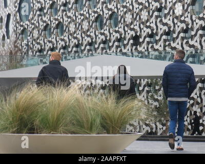 Drei junge Leute gehen auf ein auffälliges Gebäude, die gemusterten hat Mosaik Verkleidungen an den Wänden und runden Fenstern. Stockfoto