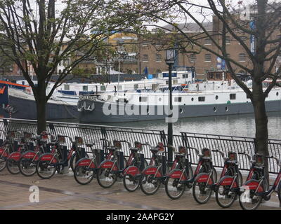 Fahrräder von Santander gesponsert, in einer Reihe von der Uferstraße an der West India Quay, mit angelegter Lastkahn Dana im Hintergrund. Stockfoto