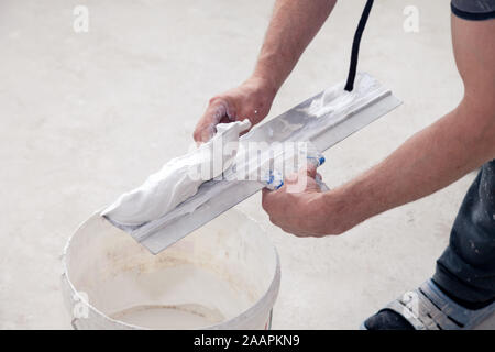 Puttyer holding Spachtel mit putty Lösung. Drinnen Bauarbeiten Konzept. Builder setzen dekorative Zementputz zu Kelle in Bau bucke Stockfoto