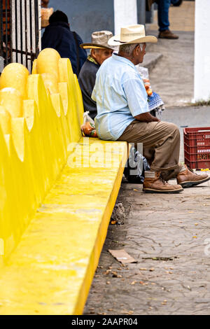 Ältere mexikanischen Männer sitzen auf einem hellen Gelb Bank in einem Park in Santiago Tuxtla, Veracruz, Mexiko. Stockfoto