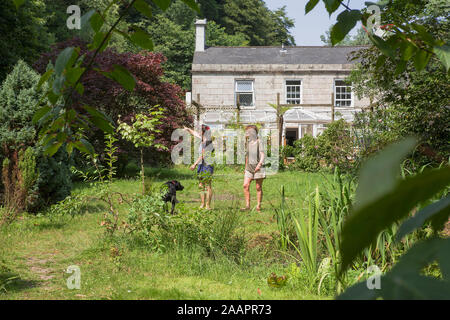 Zwei Frauen und ein Hund bewundern den wilden Garten des Waterwheel Inn in der Nähe von St. Austell, Cornwall, Großbritannien. MODELL VERÖFFENTLICHT Stockfoto
