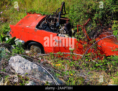 ORANGE CRUSH – Ein Sportwagen ( Triumph Herald Sports 1960?) Verrottet in der spanischen Sonne, nachdem sie in einer unzugänglichen Position zur Ruhe gekommen ist. Die Natur hüllt sie langsam mit Pflanzen, Kakteen und Unterholz ein Stockfoto