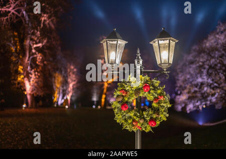 A Christmas wreath hängend auf einer Straße Licht, mit violettem Licht der Weihnachtsbeleuchtung im Hintergrund Bäume Stockfoto