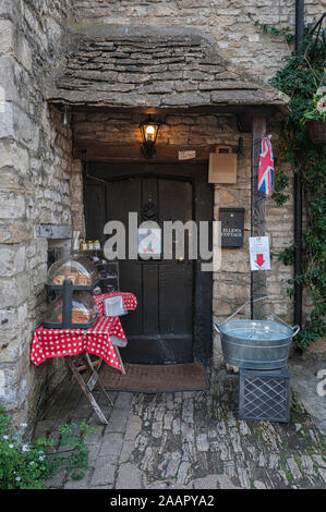 Schöne Vorderseite des alten Steinhauses mit einem Tisch, der hausgemachte Kuchen im malerischen Castle Combe Village, Chippenham, Cotswolds verkauft Stockfoto