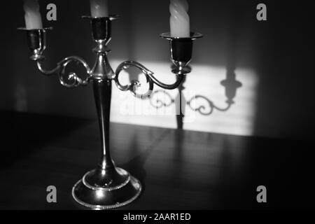 Vintage Leuchter für drei Kerzen mit Schatten Reflexion an der Wand. Schwarz-weiß Foto. Stockfoto