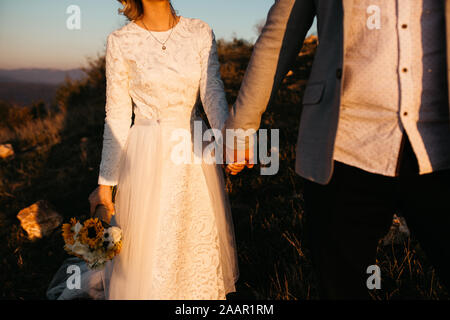 Wunderschönes Paar, das einen romantischen Moment an ihrem Unkraut, in den Bergen bei Sonnenuntergang, hat. Miteinander laufen. Die Frau ist in einem weißen Hochzeitskleid. Stockfoto