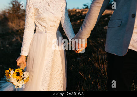 Wunderschönes Paar, das einen romantischen Moment an ihrem Unkraut, in den Bergen bei Sonnenuntergang, hat. Miteinander laufen. Die Frau ist in einem weißen Hochzeitskleid. Stockfoto