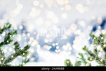 Blurry schneereiche Winter oder Weihnachten Hintergrund mit Tannen Zweigen und glühenden kreisrunden Licht Stockfoto