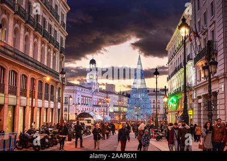 Puerta del Sol Platz bei Einbruch der Dunkelheit durch die Weihnachtsbeleuchtung und ein glänzender Weihnachtsbaum beleuchtet. Blick von Alcala Straße. Stockfoto