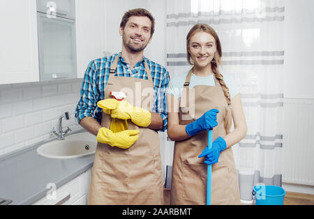 Junger Mann und Frau in Schürzen mit Hausrat posiert inmitten einer leichten Küche Stockfoto